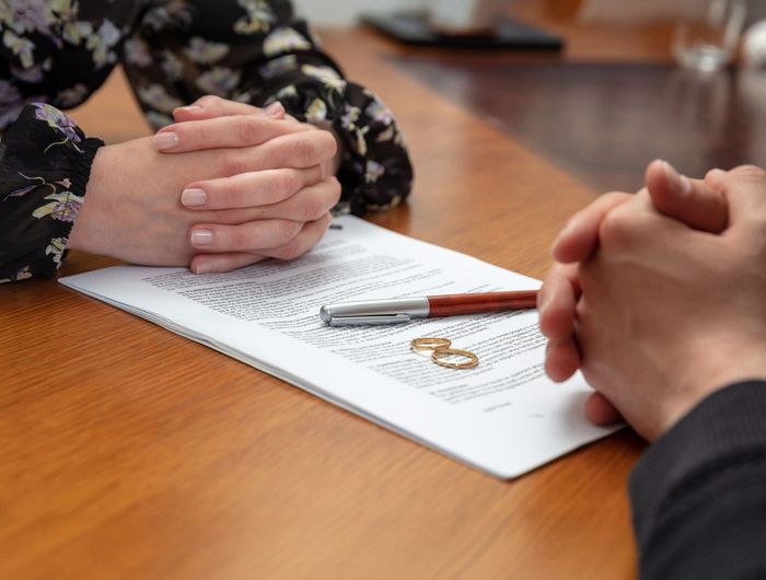 A man and a woman are sitting at a table with their hands folded over a piece of paper with wedding rings on it. A man and a woman are sitting at a table with their hands folded over a piece of paper with wedding rings on it.