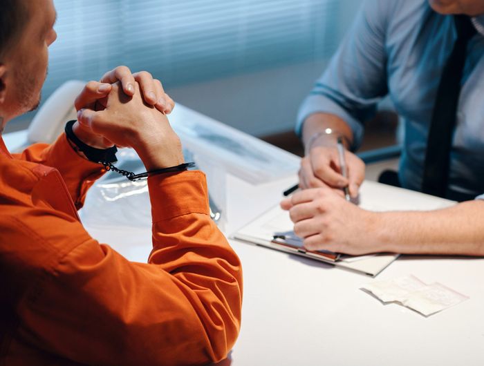 A man in handcuffs is sitting at a table with a man in a suit. A man in handcuffs is sitting at a table with a man in a suit.