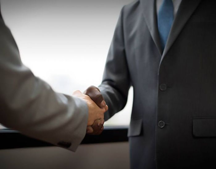 Two men in suits are shaking hands in an office. Two men in suits are shaking hands in an office.