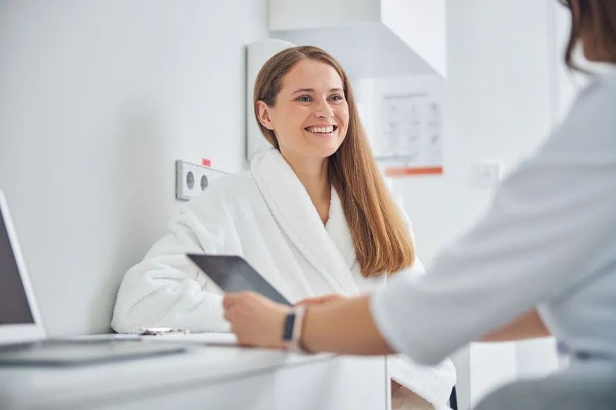 A woman in a bathrobe is sitting at a table talking to an electrolysis