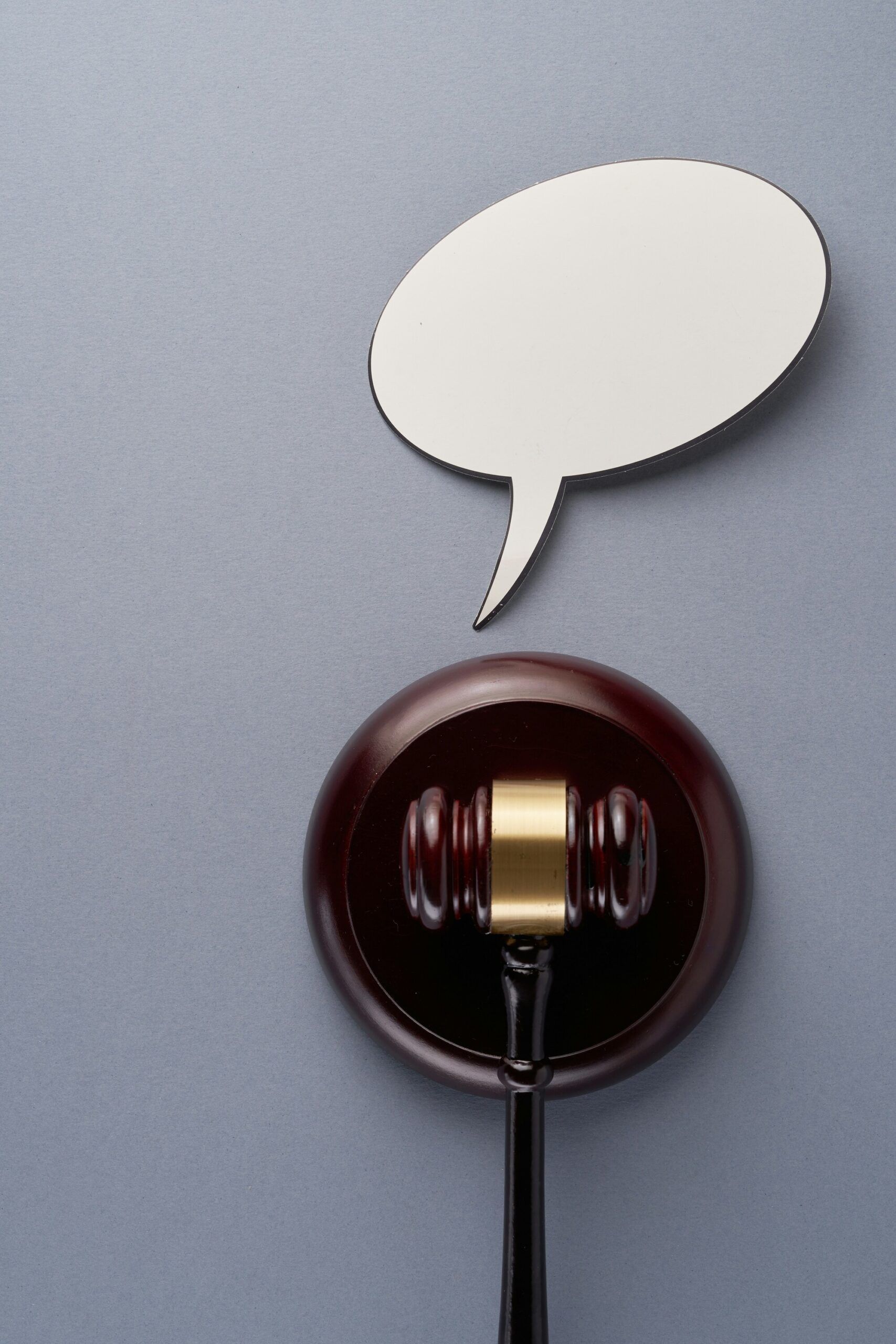 Judge’s gavel with a blank speech bubble above it on a gray background.