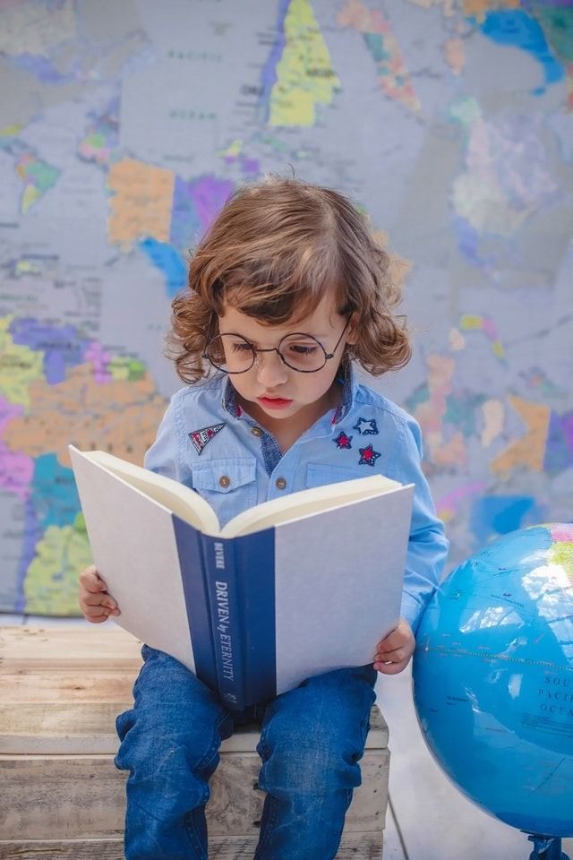 little girls in blue, sitting in bed, reading a large book, with a globe and the world map as background