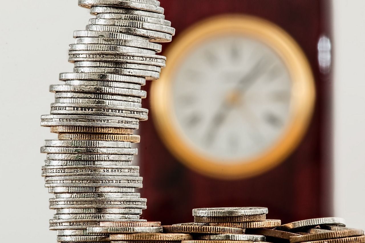 stack of coins with an out of focus clock in the background