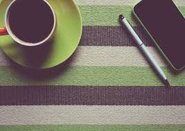 cup, green saucer, green, brown and beige table cloth, silver pen and cellphone