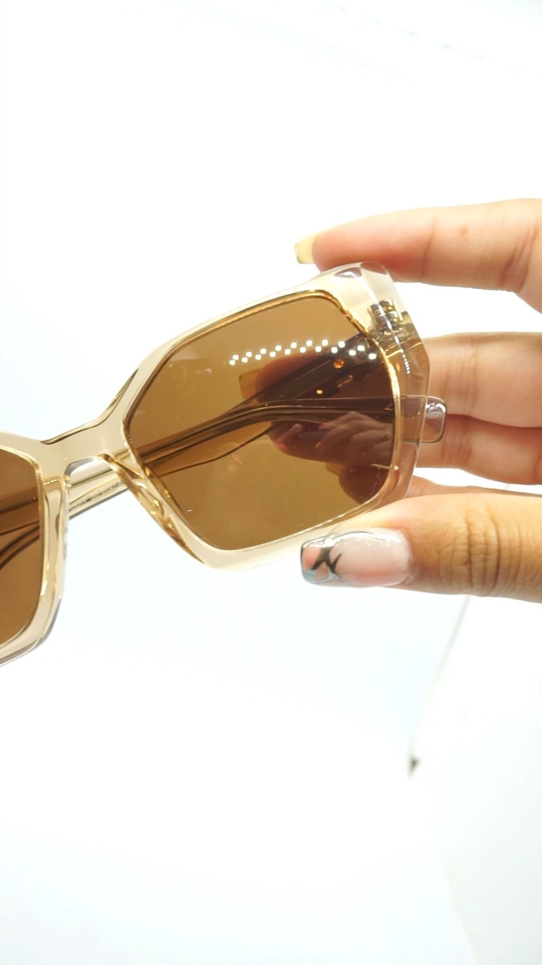 Gafas de sol con montura color canela y lentes marrones sostenidas en la mano. Fondo blanco.