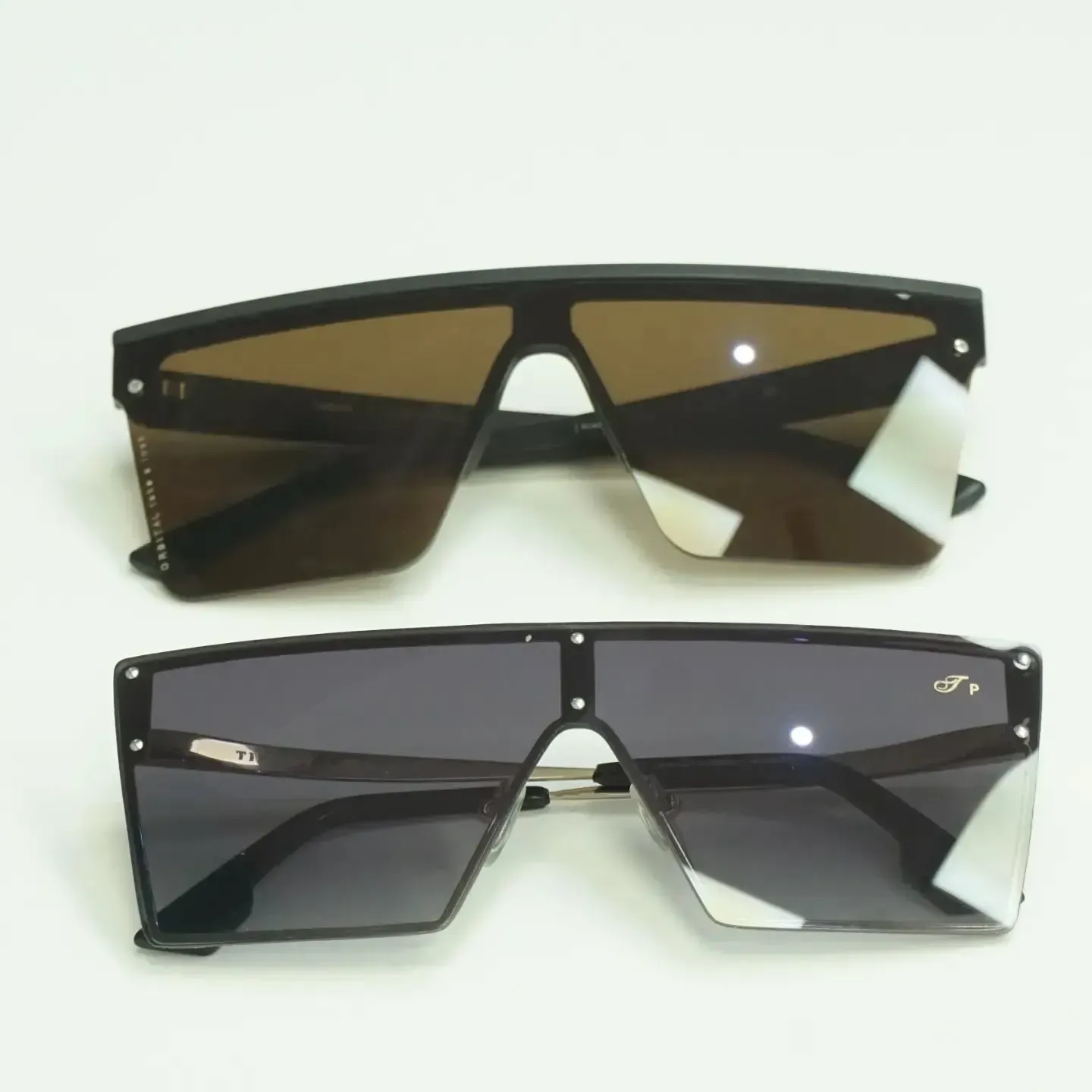 Dos pares de gafas de sol de gran tamaño con montura negra y lentes tintadas: marrón y gris.