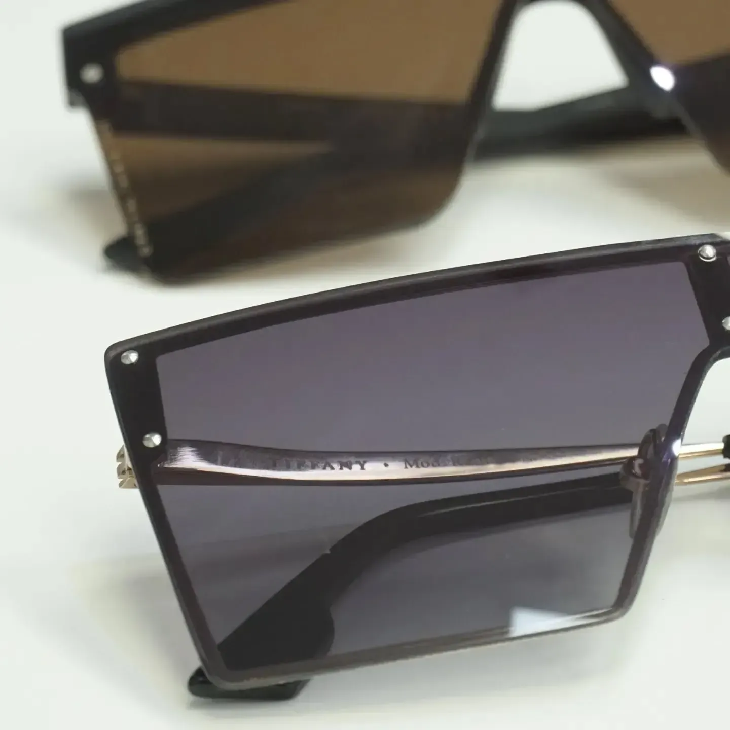 Dos gafas de sol angulares con lentes oscuras y montura negra.