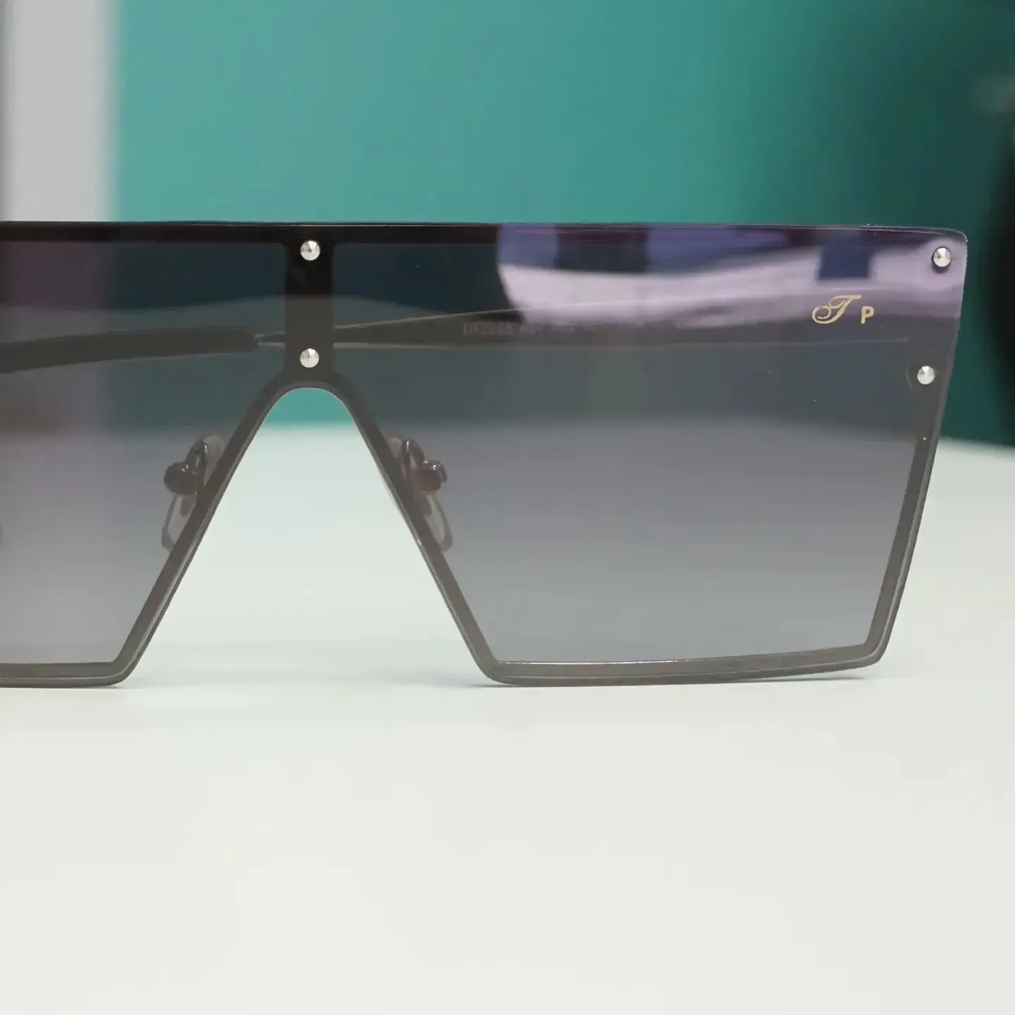 Gafas de sol de color gris oscuro, de gran tamaño y con la parte superior plana, apoyadas sobre una superficie blanca.