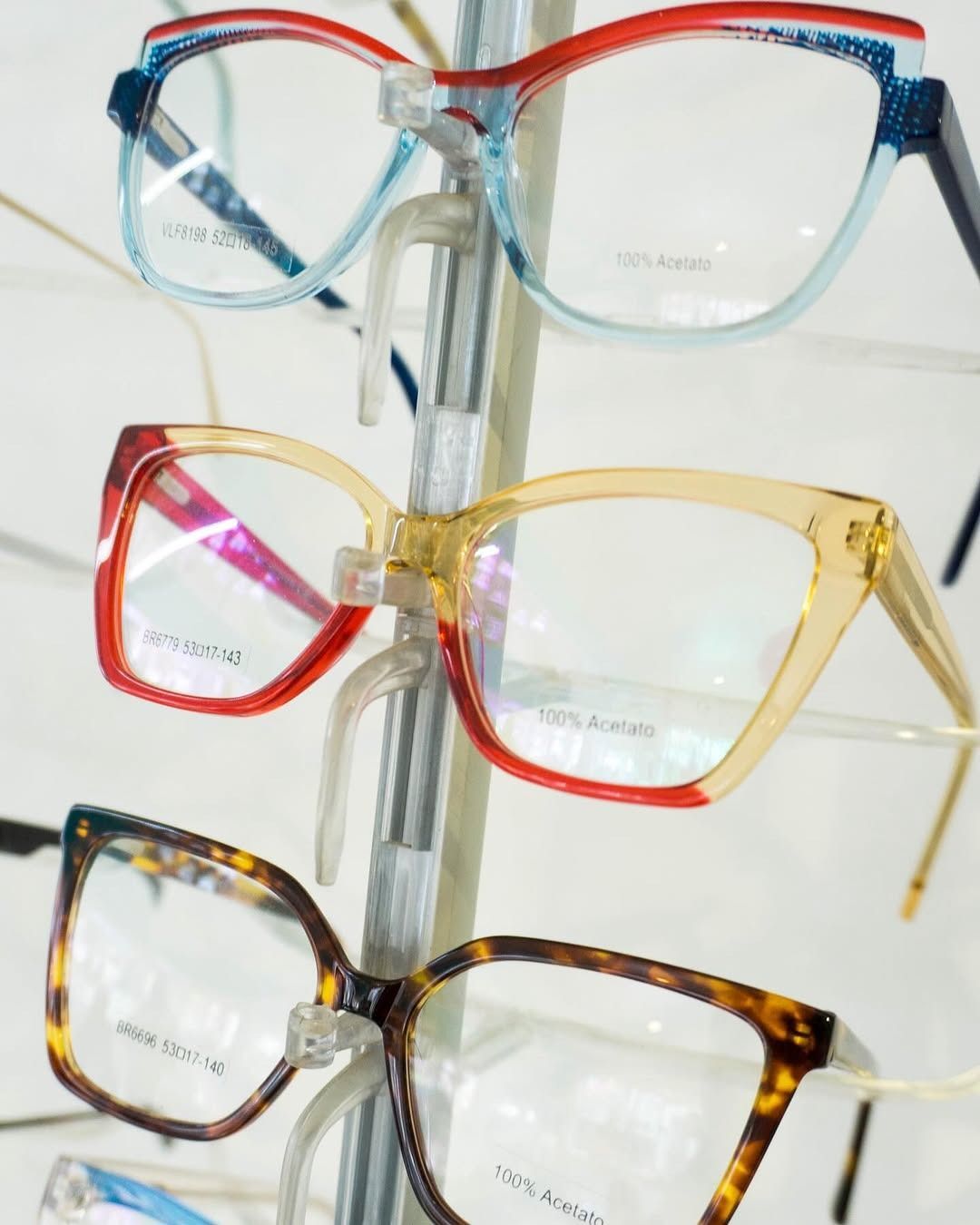 Tres pares de gafas en un expositor. Las monturas son rojo/azul, amarillo/rojo y carey.