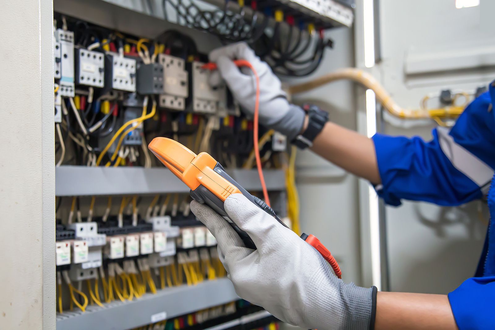 An electrician is working on an electrical panel with a multimeter.