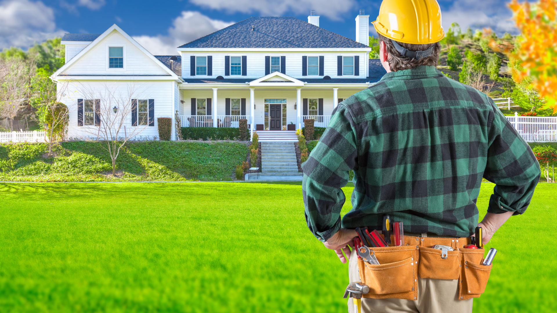 A man wearing a hard hat is standing in front of a large house.
