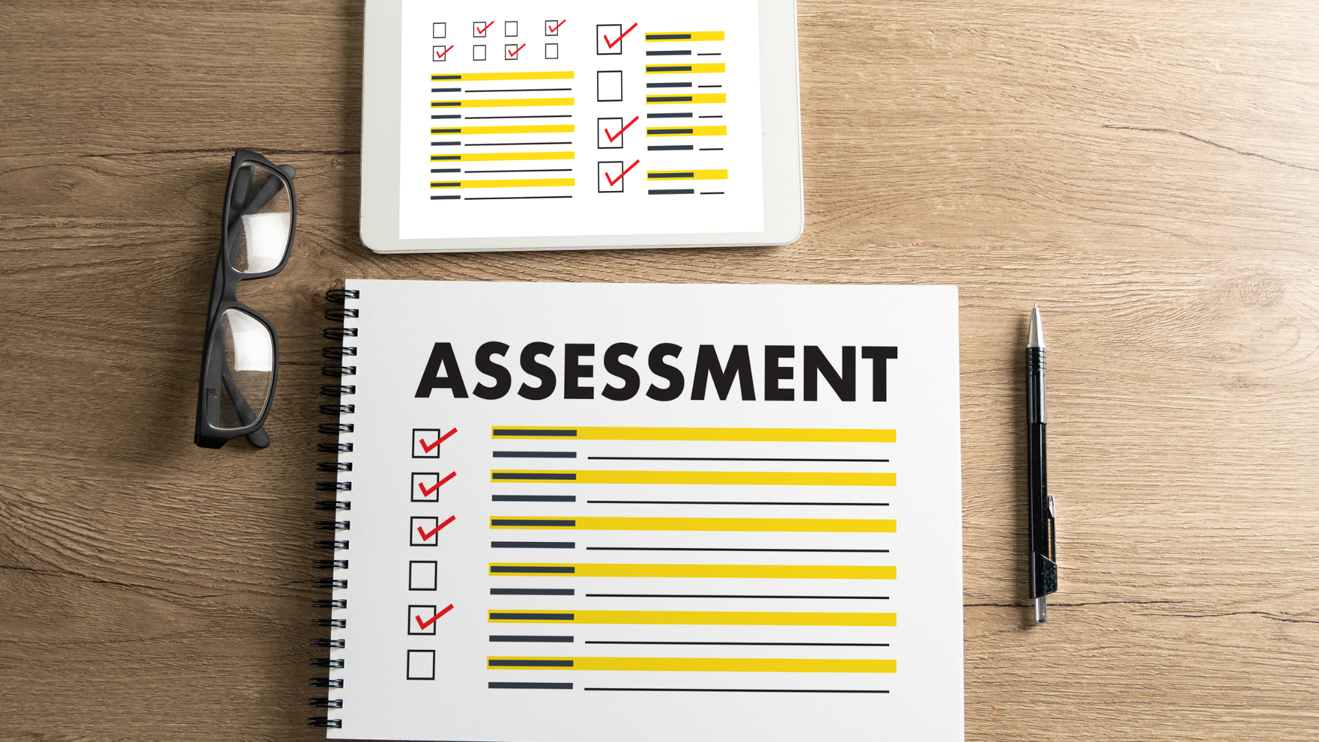 A notebook with the word assessment written on it is sitting on a wooden table.