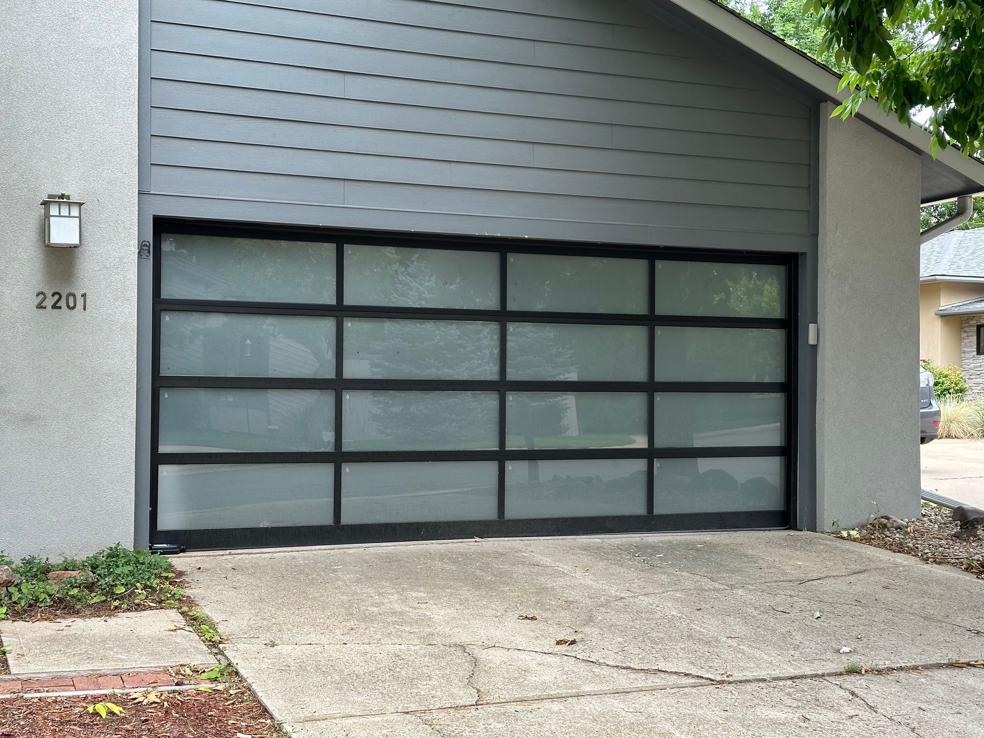 Garage with frosted glass panels and a black frame on a concrete driveway.