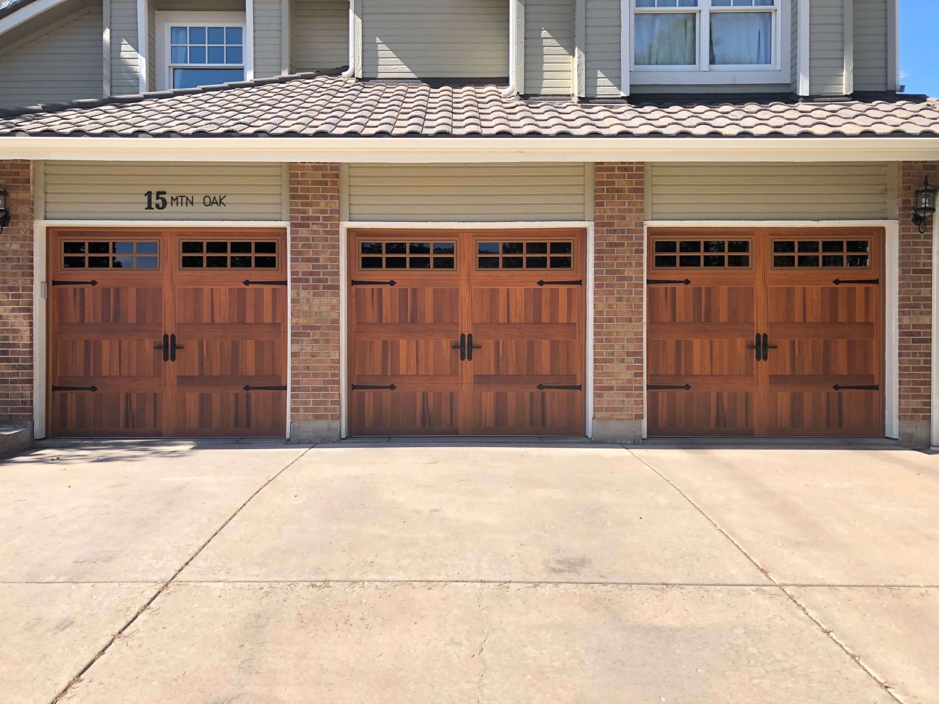 Three cedar carriage garage doors with stockton windows and deco kits , brick accents, and concrete driveway. 