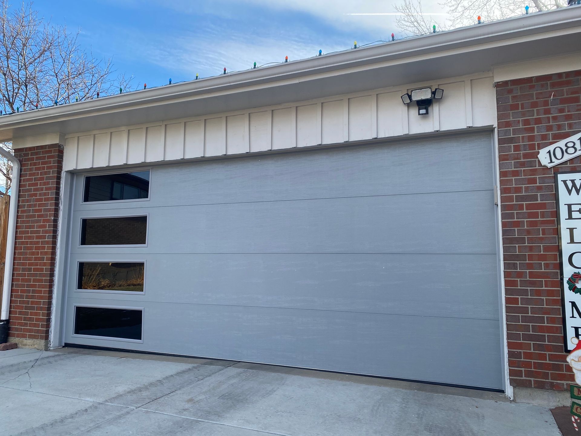 Gray garage door with glass panels; brick and white trim, blue sky.