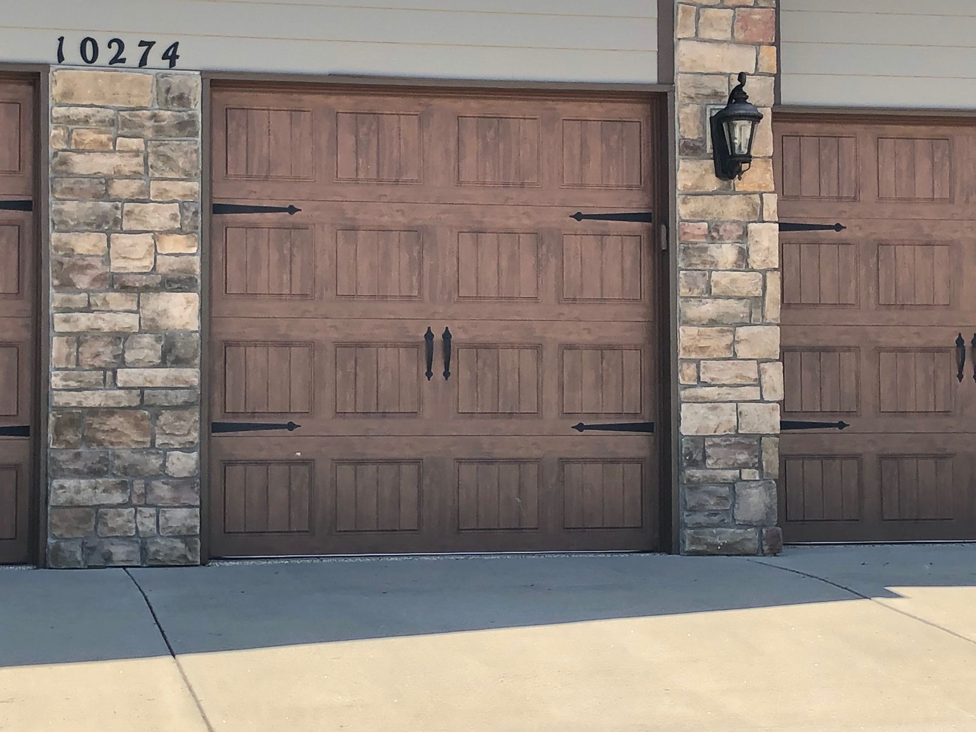 Brown wooden garage doors with black hardware and stone columns. Address 
