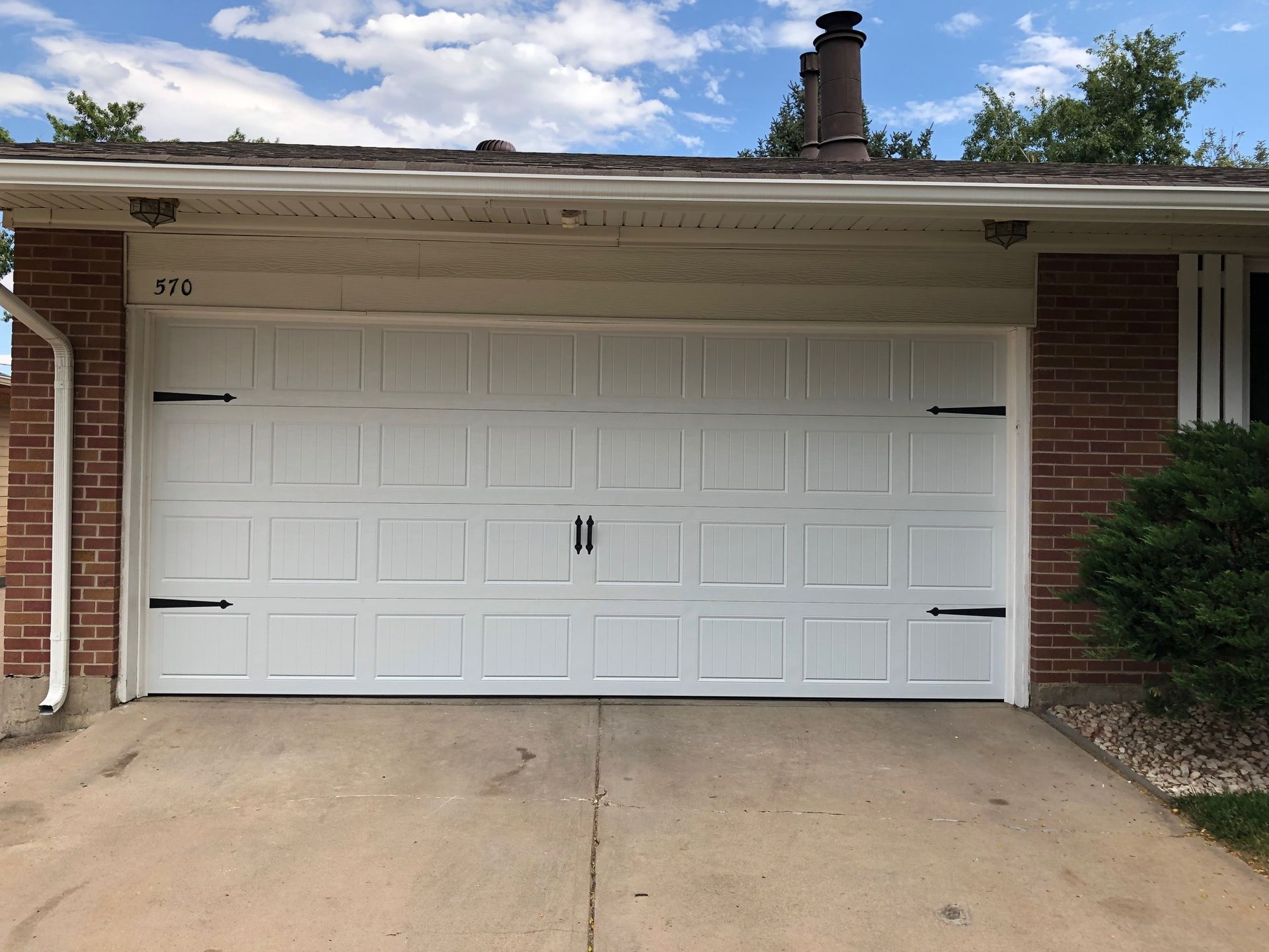 White carriage garage door with black hardware, brick accents, and a concrete driveway.