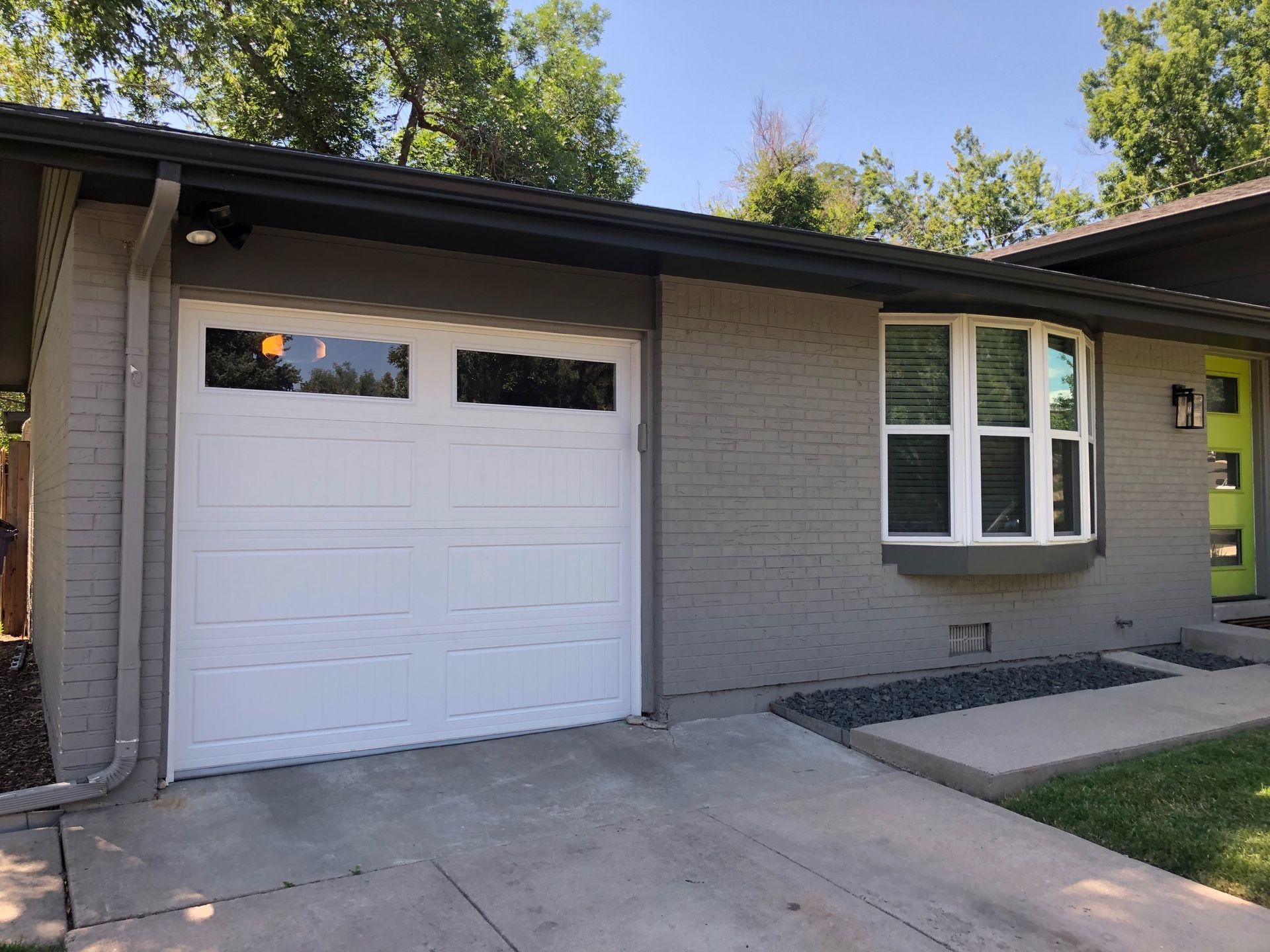 A white carriage garage door and a grey house with a bay window and a walkway.