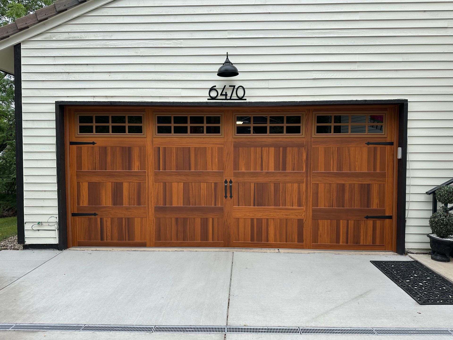 Cedar carriage garage door with stockton windows, and black lantern on a white siding house.