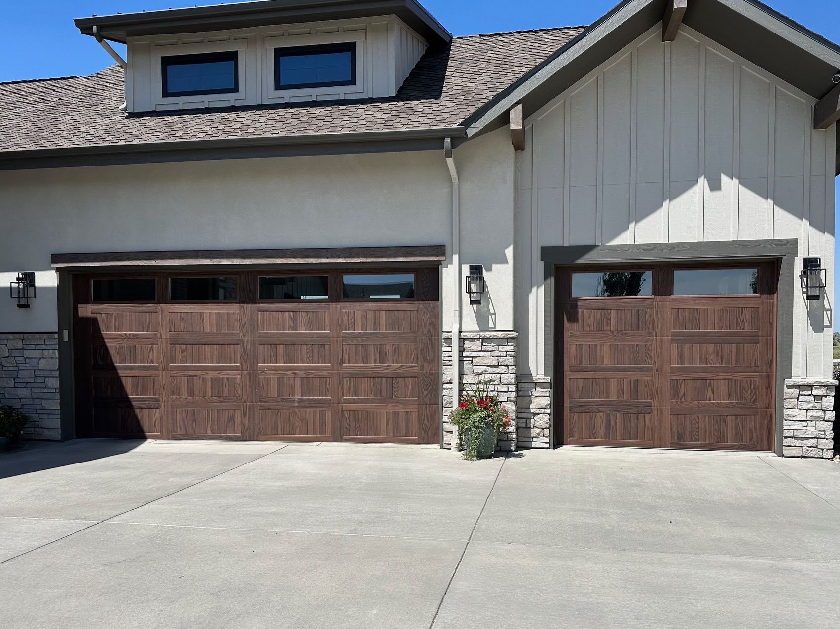 Walnut carriage garage doors with windows on a house with stone accents and a concrete driveway.