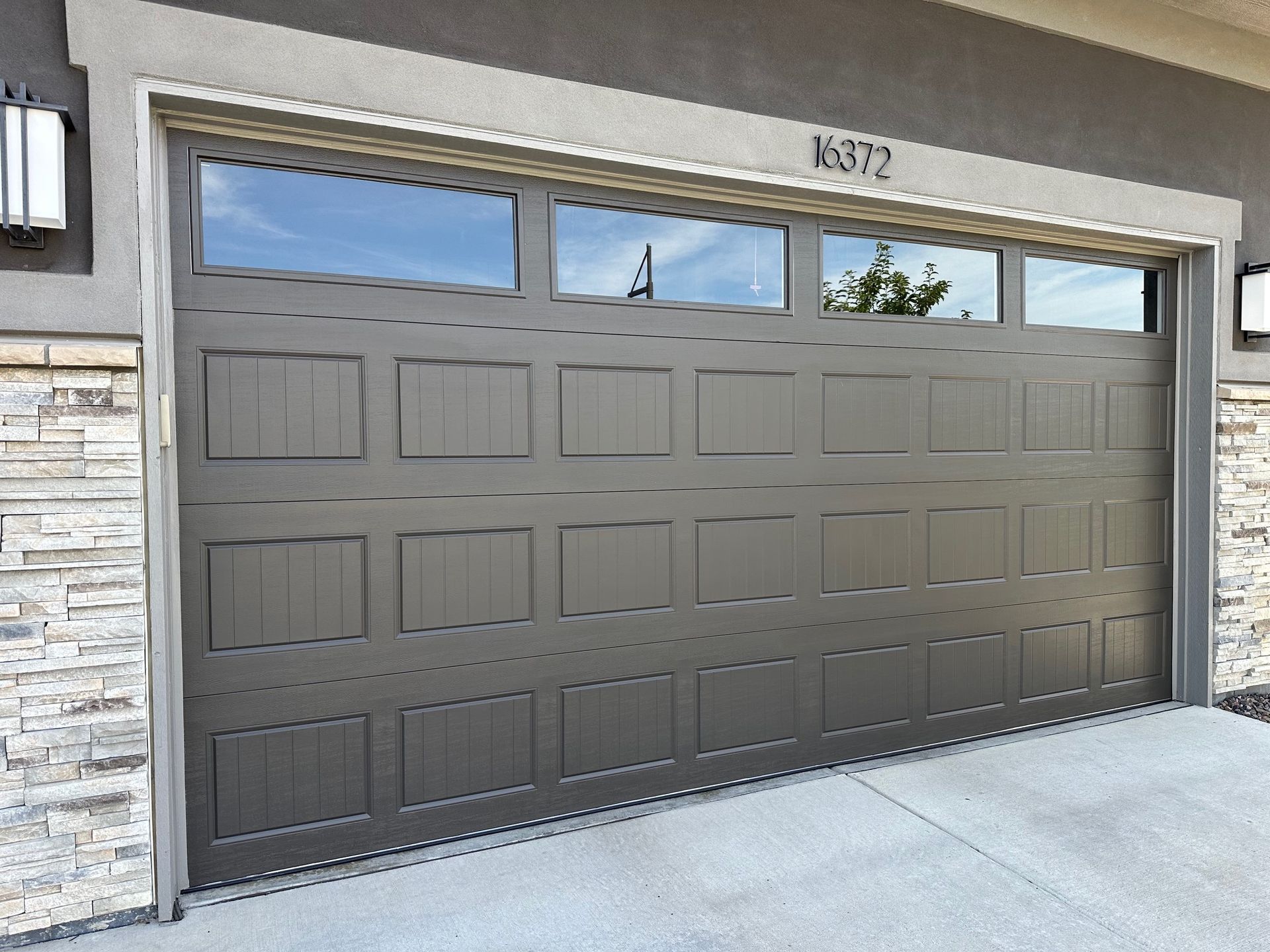 Gray carriage garage door with windows above, on a house with stone siding.