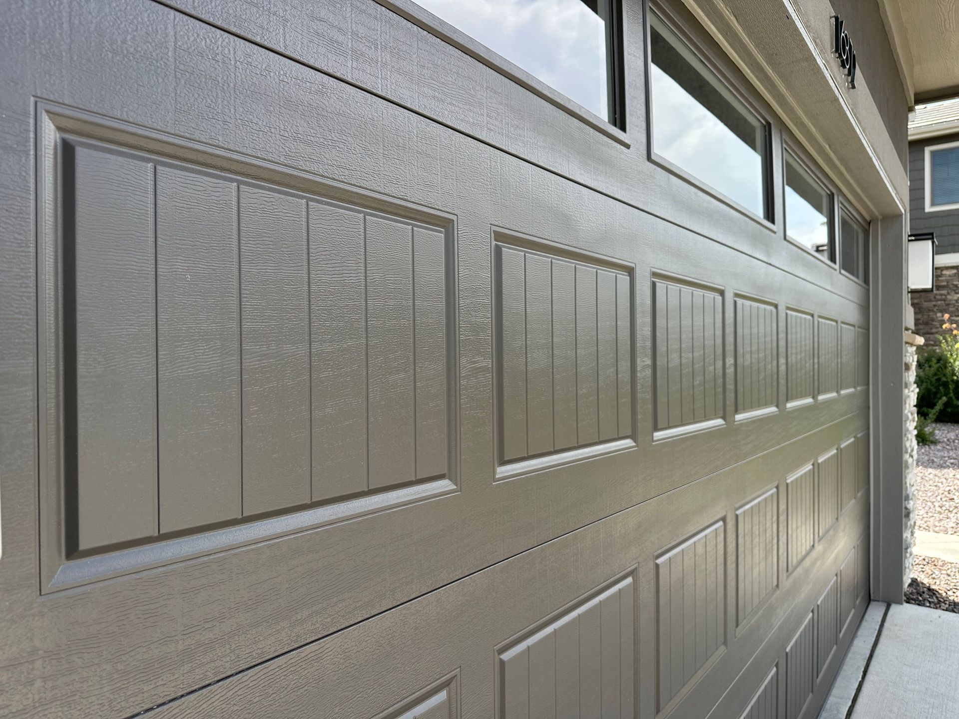 Gray garage door with rectangular panels, windows above, and light reflection.