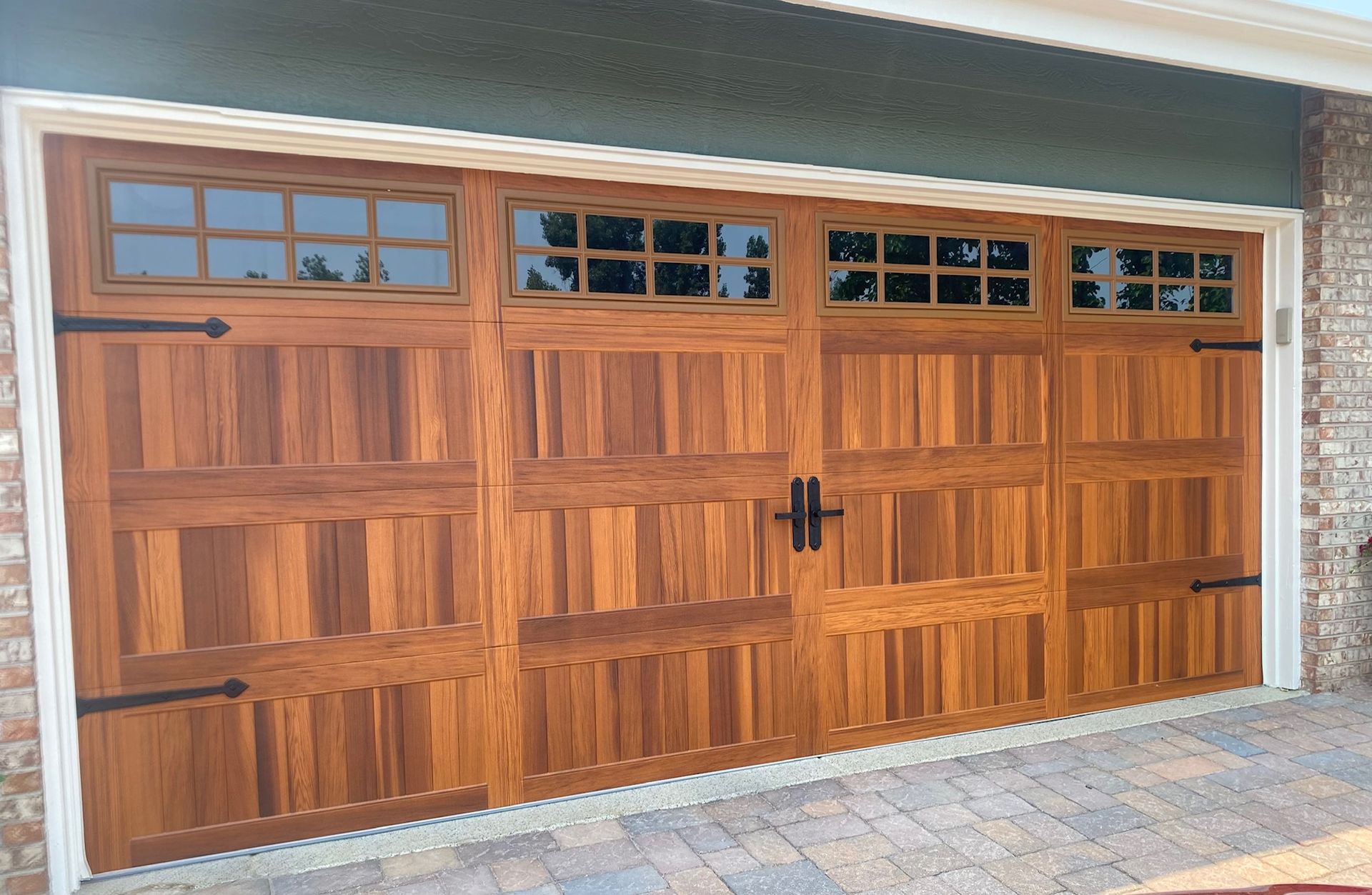 Cedar carriage garage door with stockton windows, black hardware, in a brick-lined garage entrance.