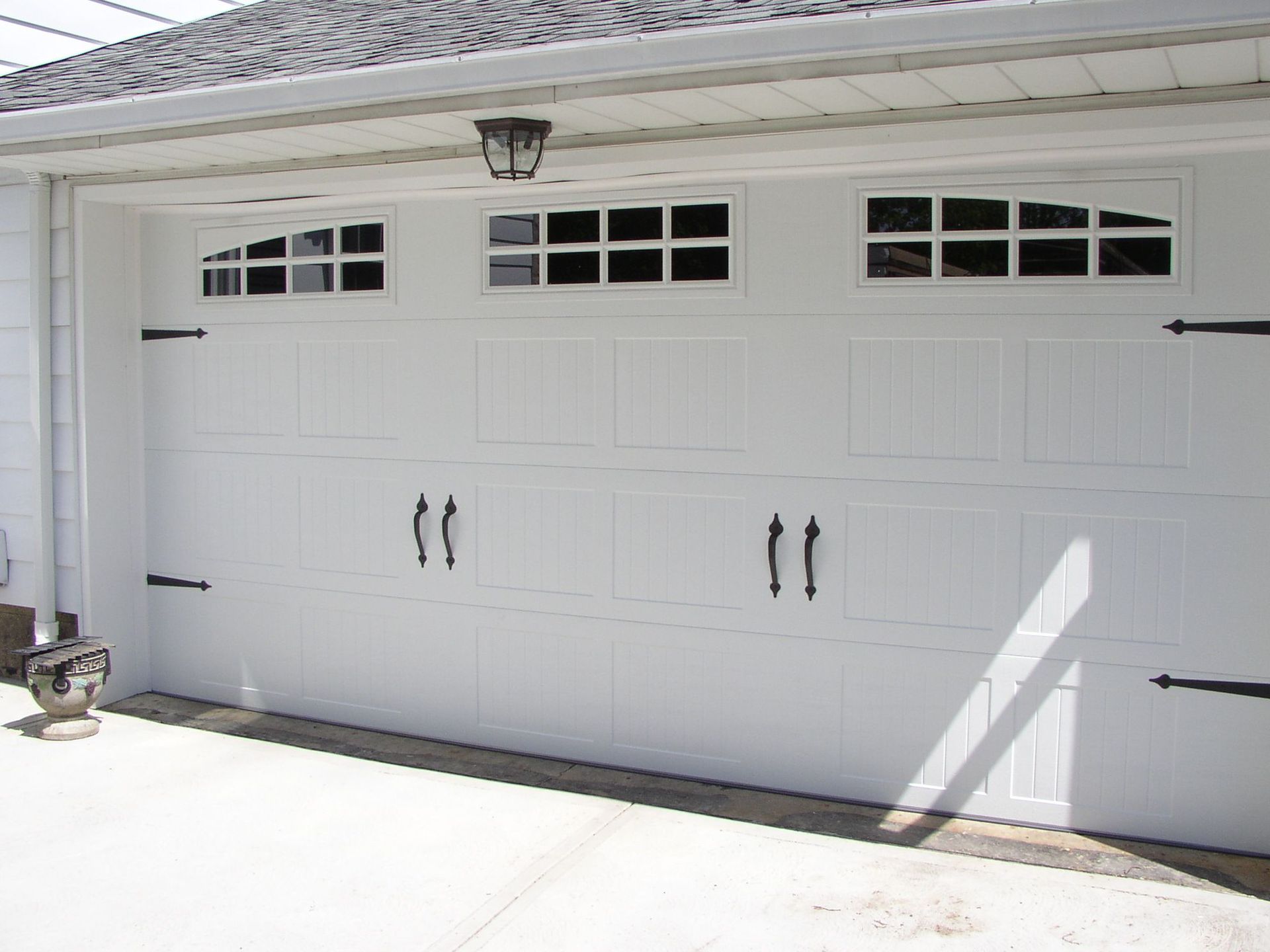 White carriage garage door with windows and black hardware, outside.