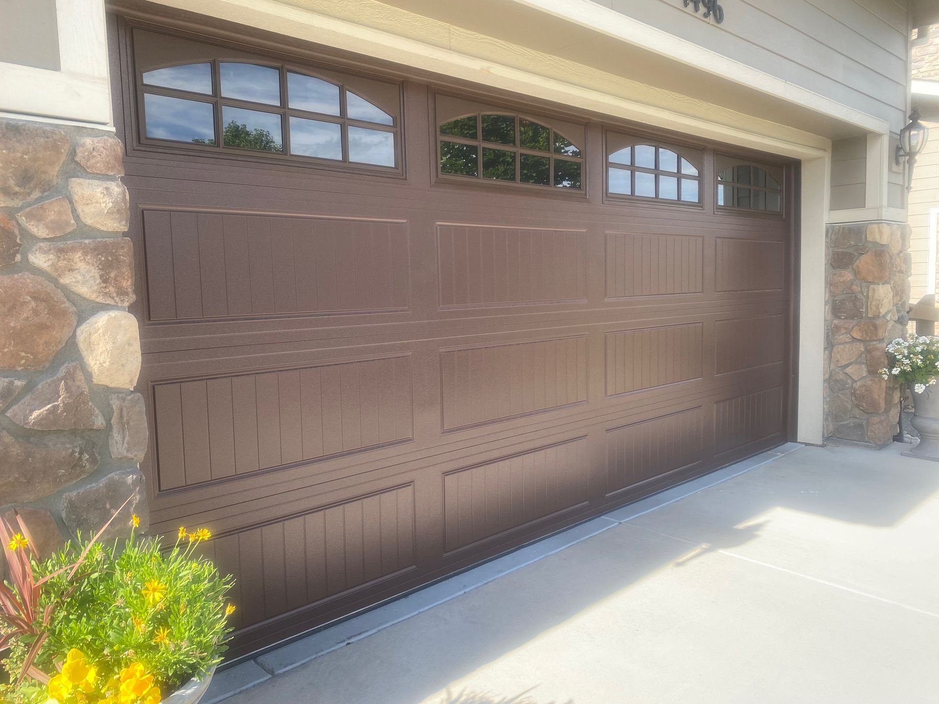 Brown carriage garage door with arched stockton windows, next to stone facade.