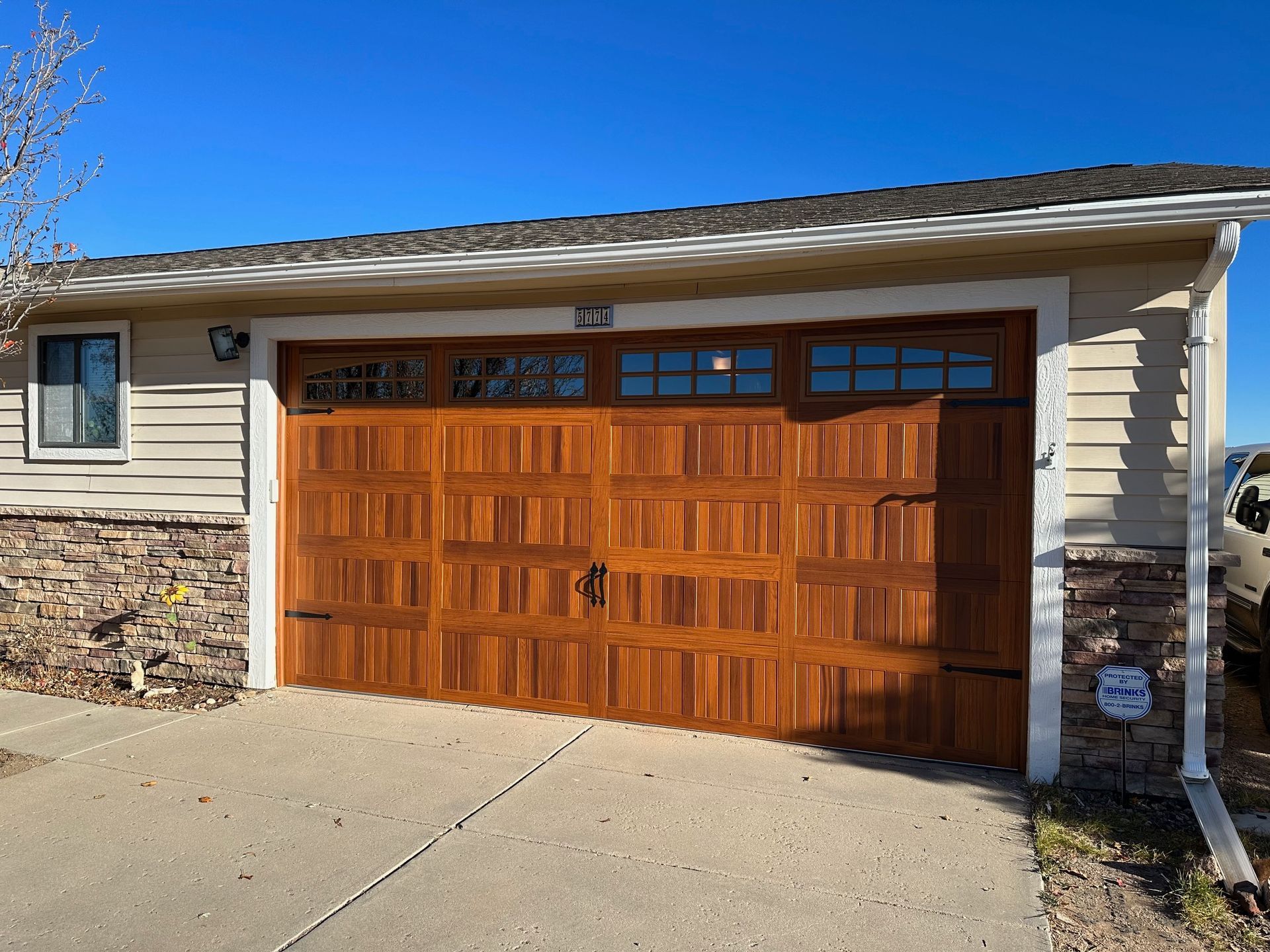 Cedar carriage garage door with stockton windows, tan siding, and stone accents against a blue sky.