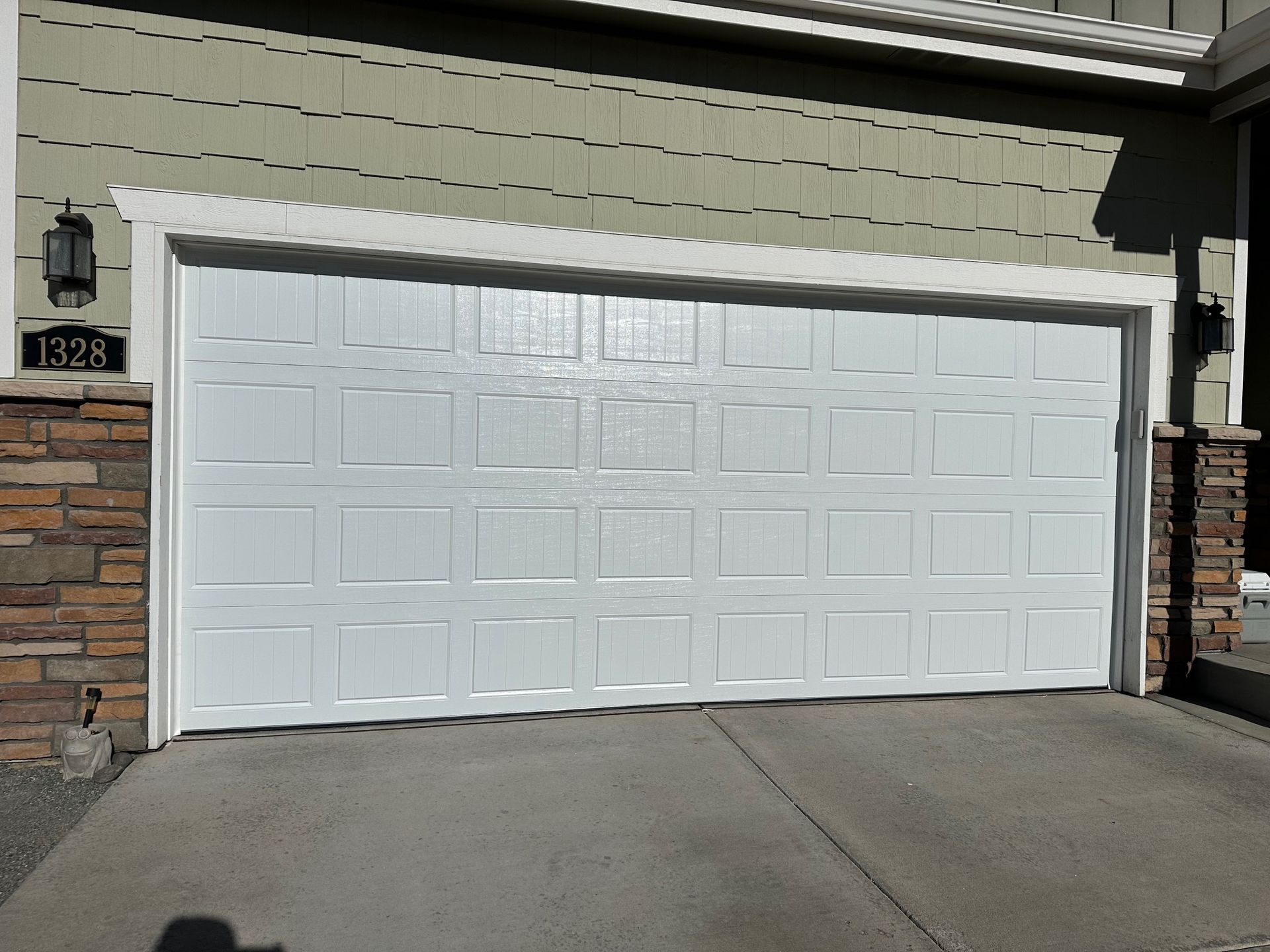 White carriage garage door on a house with stone and green siding, driveway in front.
