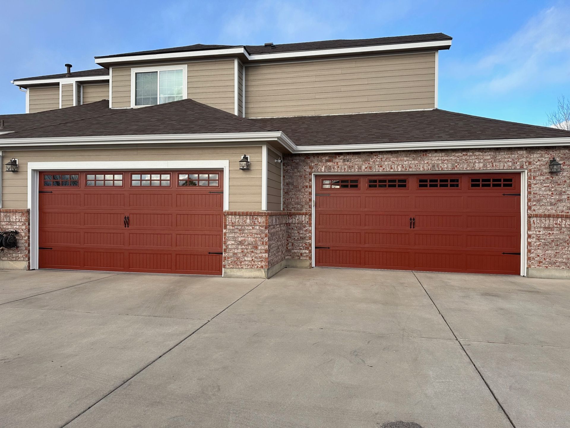 Two-story house with brick accents and two morton red carriage garage doors, concrete driveway, and a blue sky.