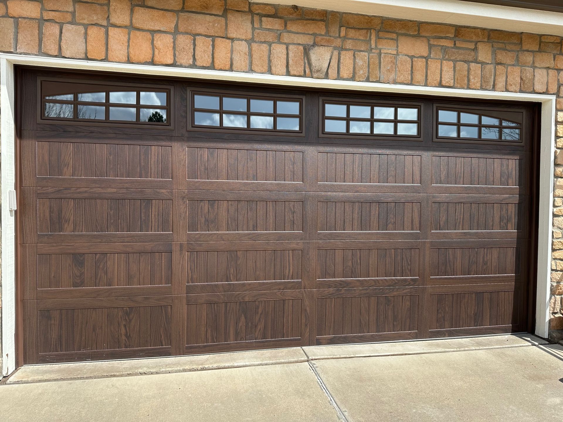 Walnut carriage garage door with somerton glass paneling set in a brick wall.