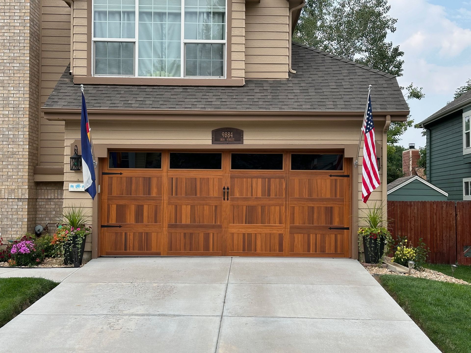 Two-car garage with cedar carriage doors, driveway, American and state flags, and house with green lawn.