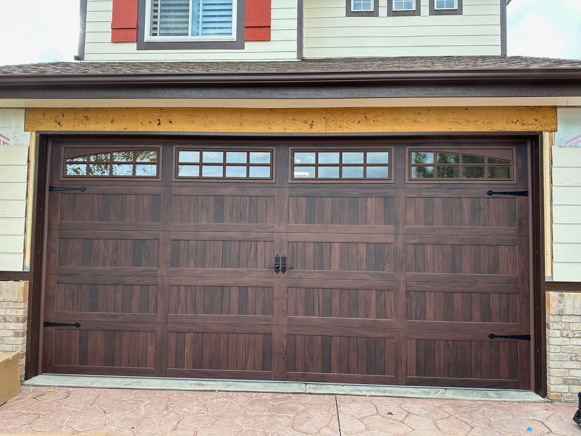 Walnut carriage garage door with windows, black hardware, and a beige house exterior.