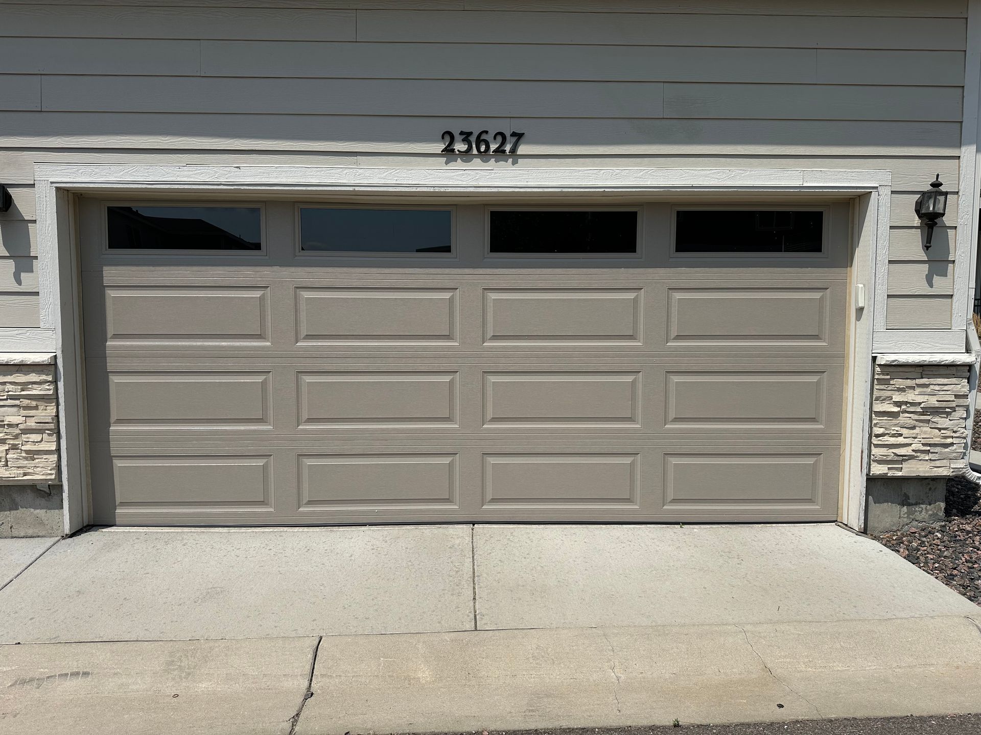 Tan garage door with windows above and a concrete driveway.