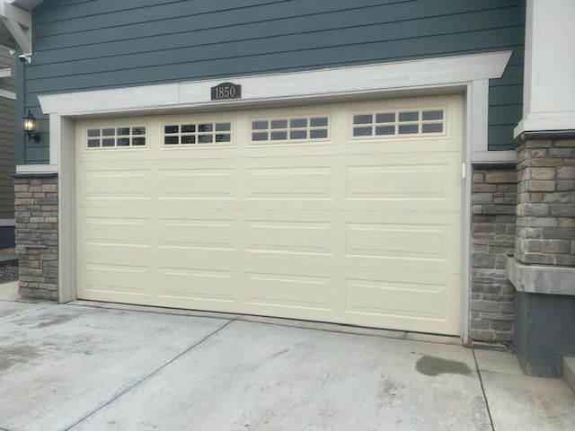 Beige garage door with small windows, blue siding above, and stone columns.