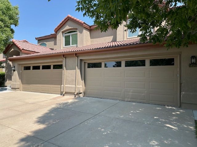 Tan two-story house with matching garage doors. Concrete driveway, red tile roof, and sunny day.