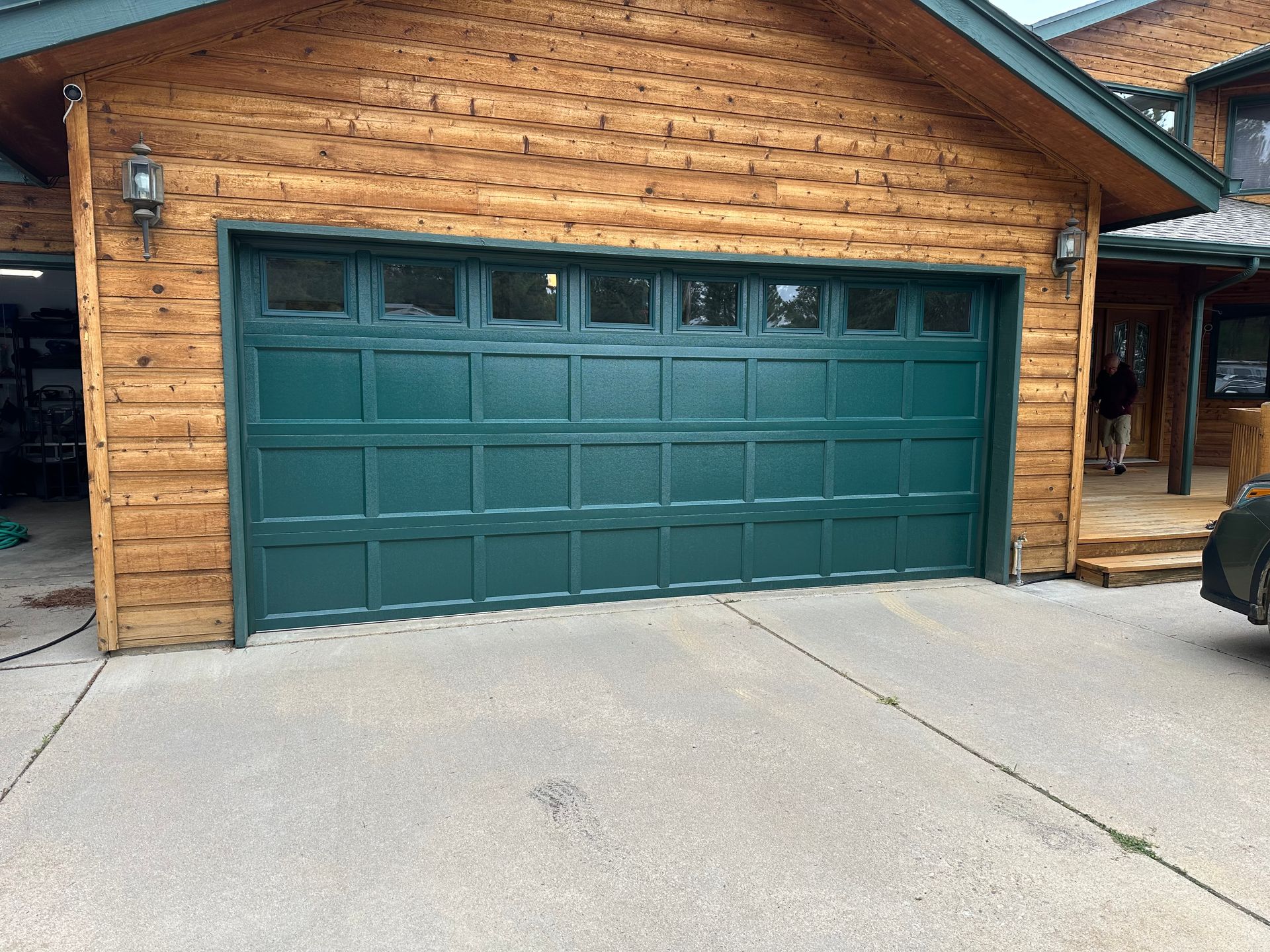 Green garage door on a log cabin home. Gray concrete driveway.