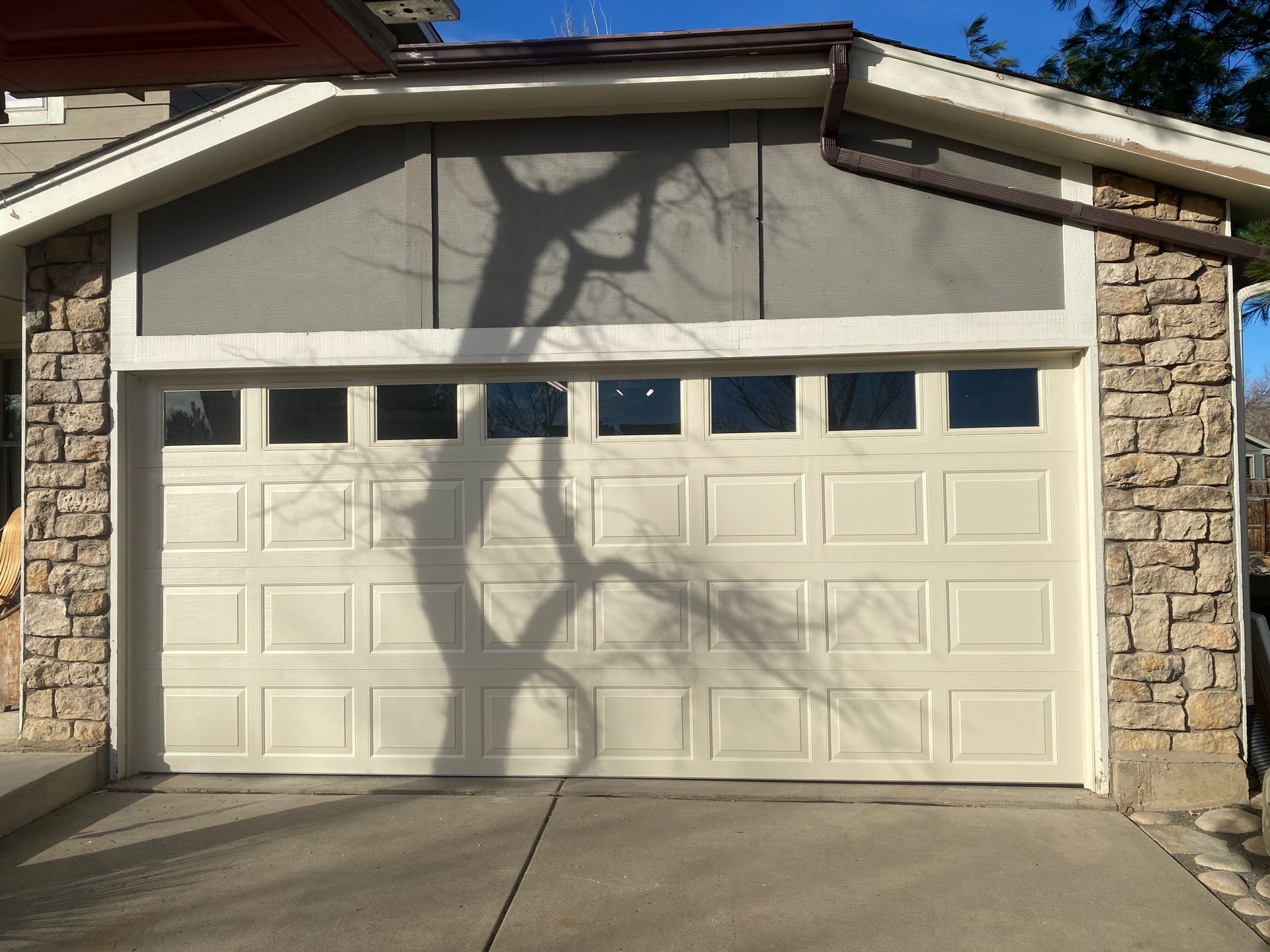 Garage with beige door, stone accents, and a tree shadow.