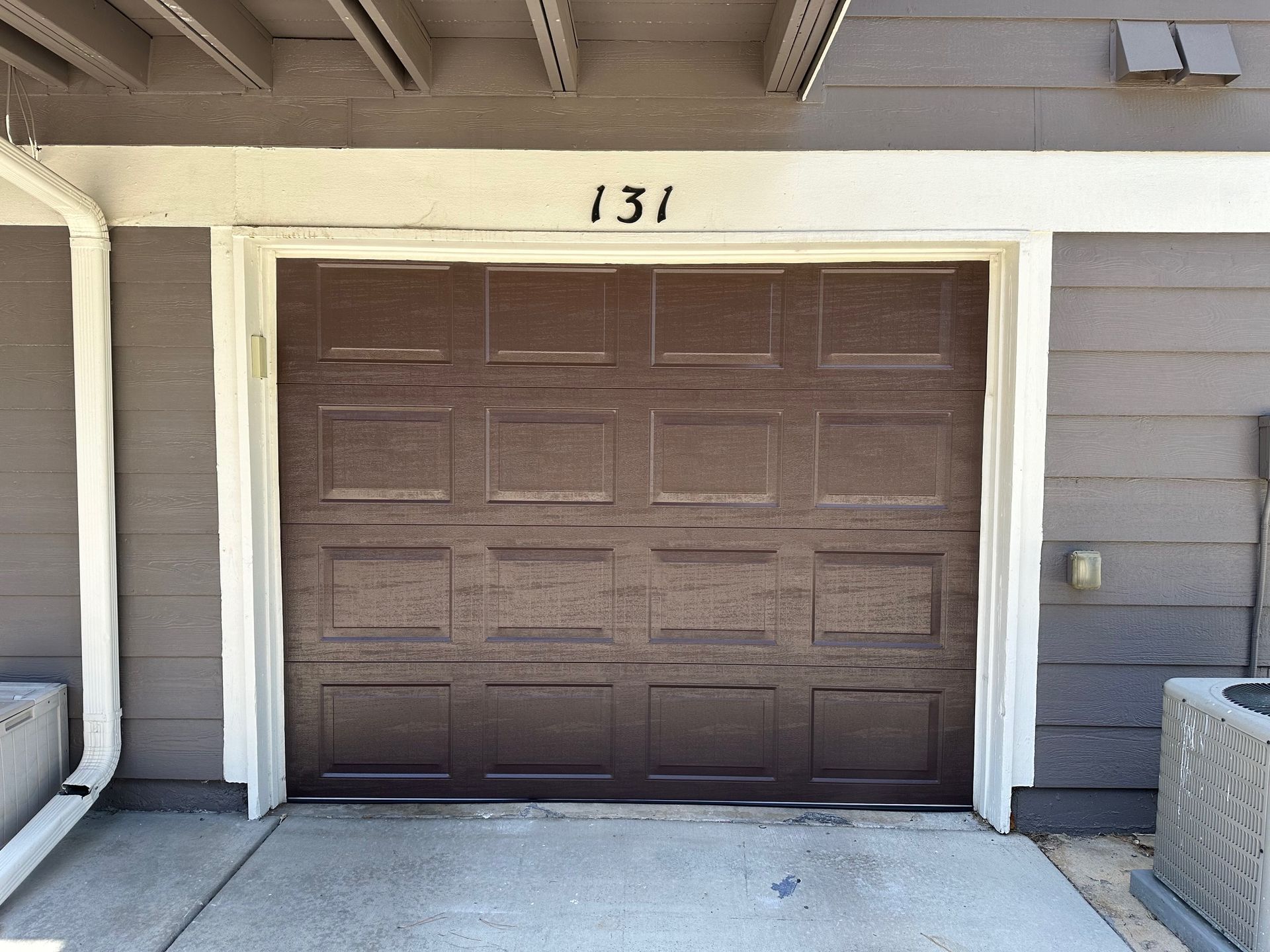 Brown garage door with the number 131 above, next to a concrete walkway.