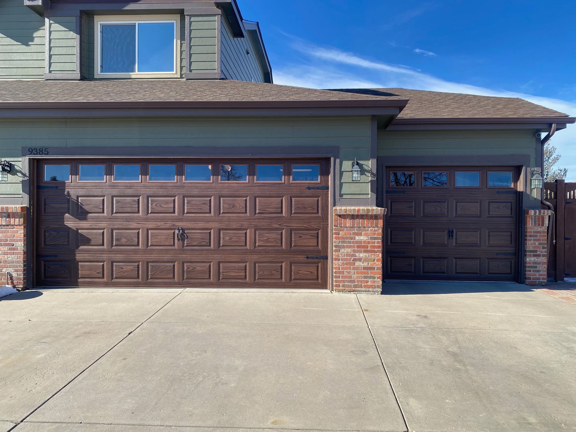 Brown garage doors with glass panels, brick accents, and a concrete driveway.
