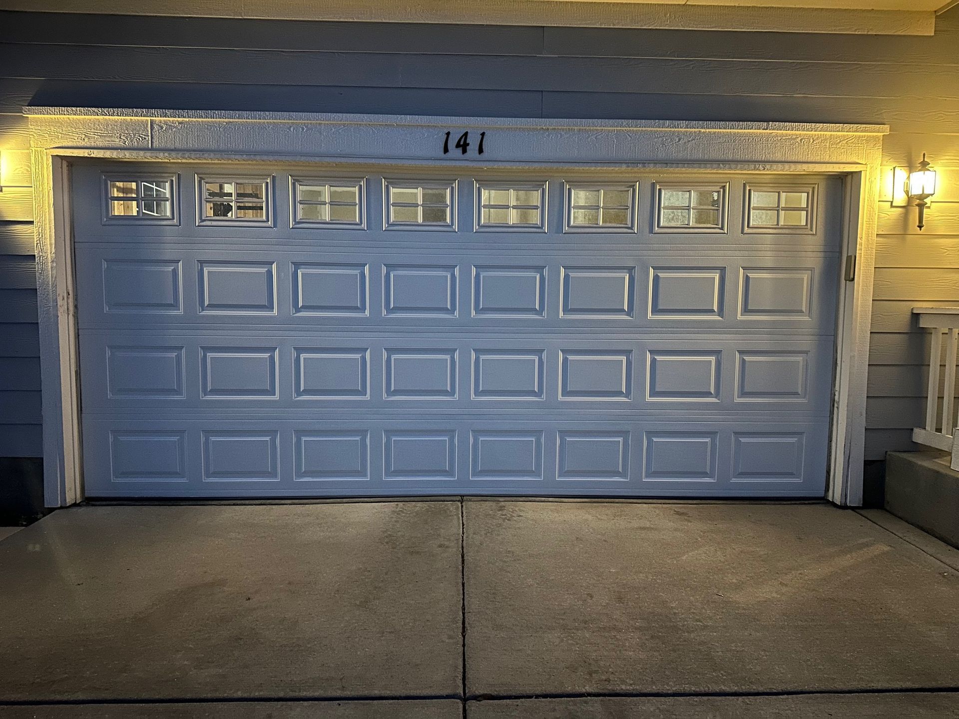 Gray garage door with windows, illuminated by warm lights, with the number 141 above.