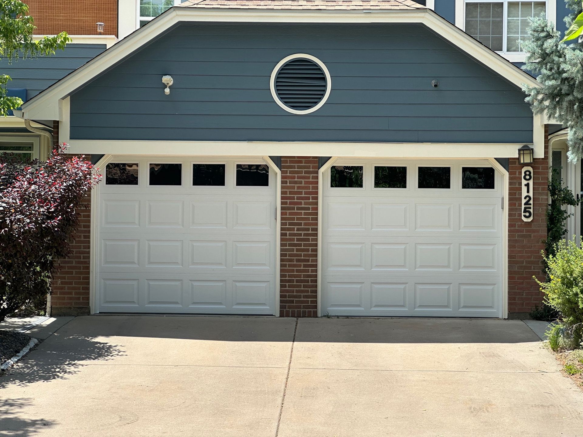 Two white garage doors on a blue house with brick accents, driveway.