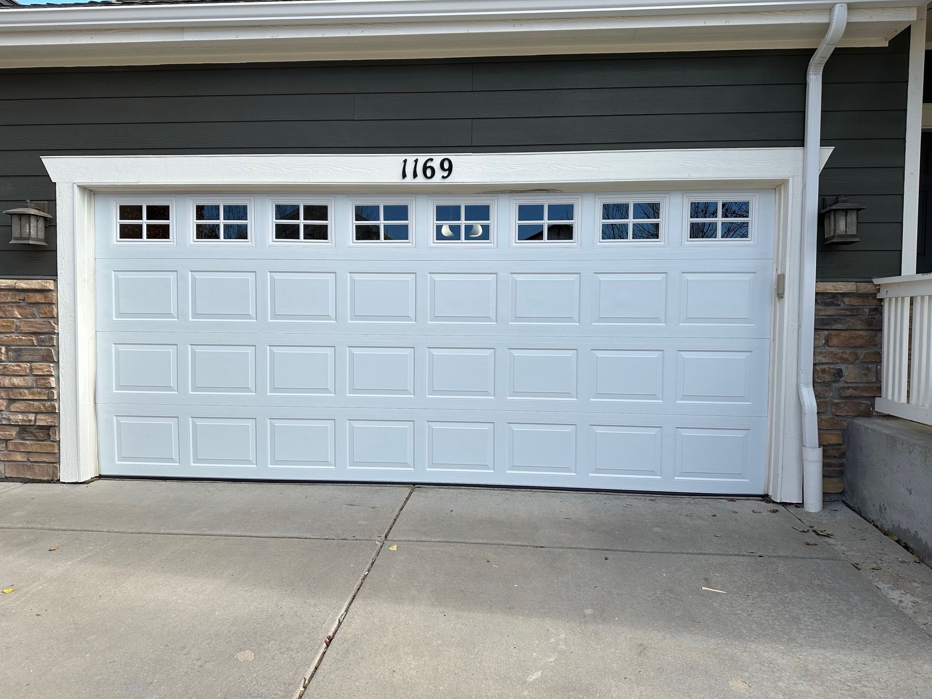 White garage door with windows, address 1169 above, on a house with stone and green siding.
