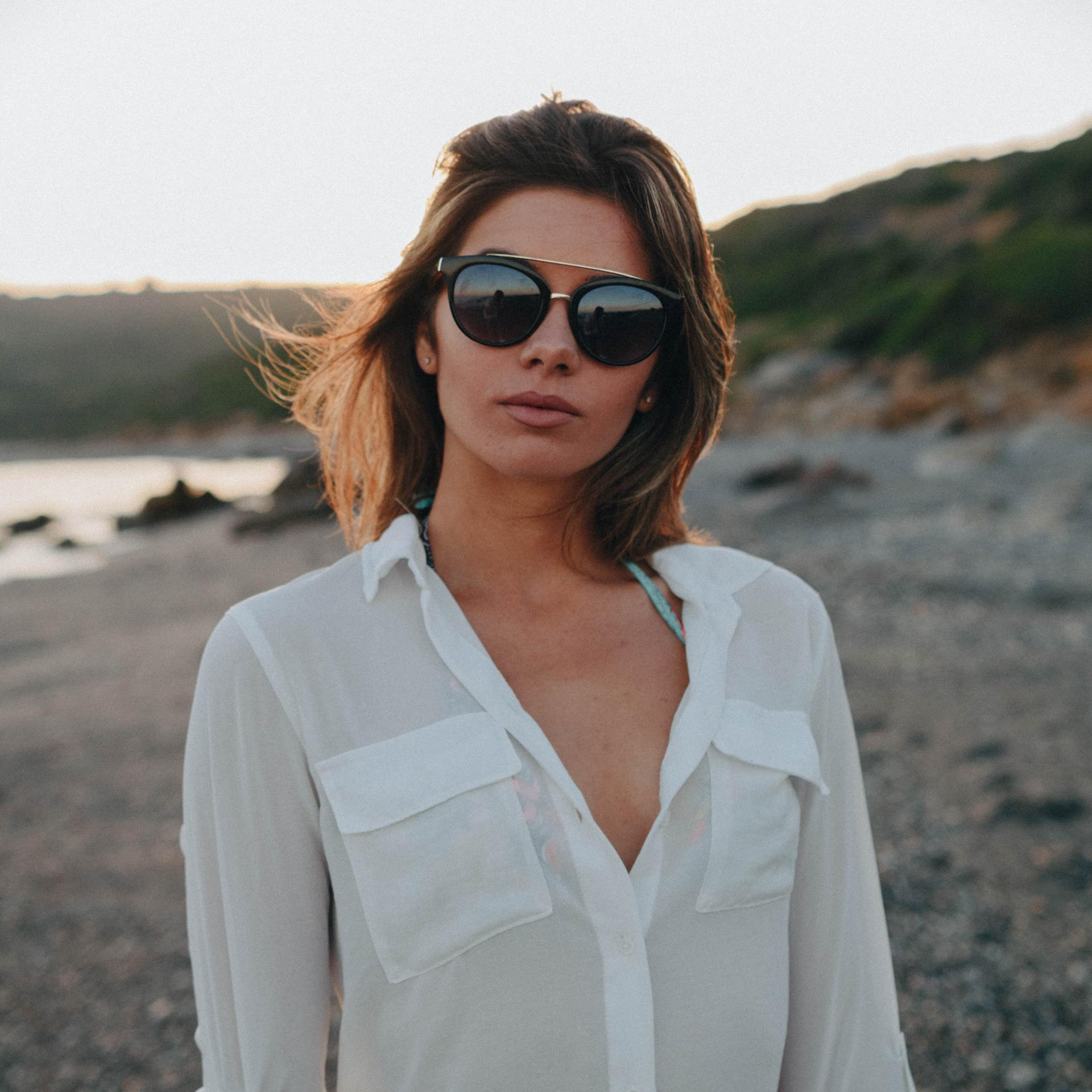 Attractive brunette wearing sunglasses and white shirt at the beach after sunset