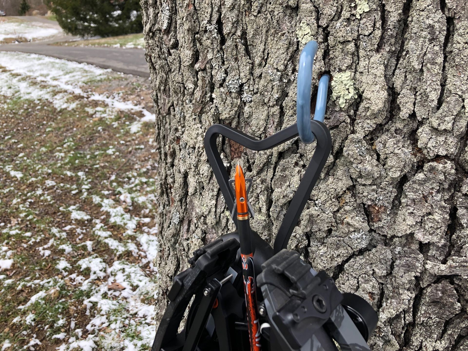 A Ravin Crossbow with the Heart Drop Hanger hanging from a hook on a tree.