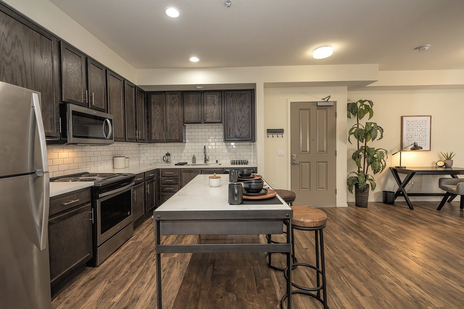 Apartments for Rent El Cerrito, CA - Metro 510 - Spacious Kitchen with Stainless Steel Appliances, Dark Wooden Cabinetry, White Tile Backsplash, White Countertops, Large Island with Stool Seats, and Wood-Style Flooring