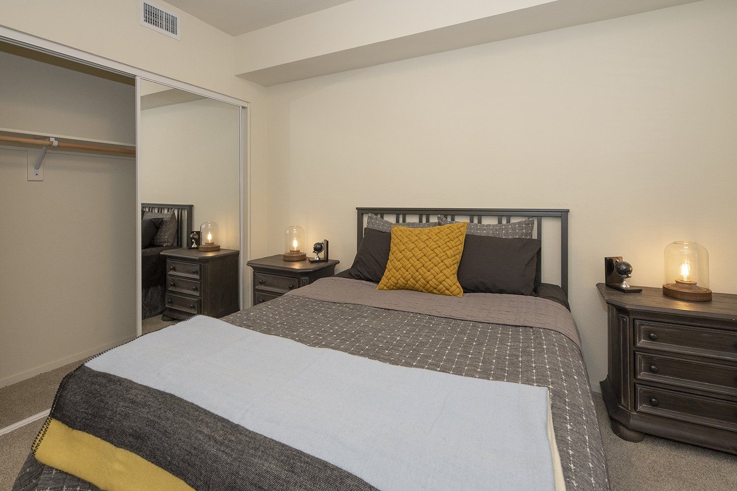 Studios in El Cerrito CA - Metro 510 - Bedroom With Plush Carpet Flooring, High Ceilings, Two Matching Wooden Nighstands, Beige Walls, and a Spacious Closet With Mirror Sliding Doors