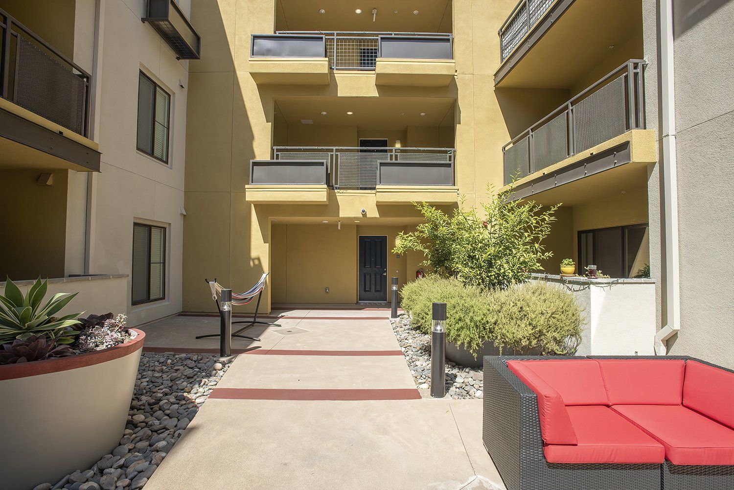 El Cerrito Apartments - Metro 510 - Courtyard In The Heart Of The Complex. The Courtyard Has Plush Seating, Stools, Lights, Potted Plants, And Maintained Landscaping.
